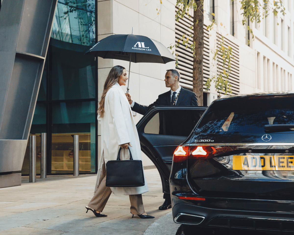 Woman getting into an Executive Addison Lee taxi while a chauffeur holds an umbrella for her and opens thecar door