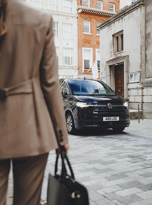 A woman from behind holding a briefcase with an Addison Lee mutlivan in the background
