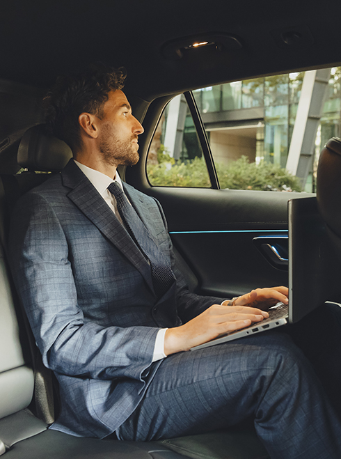 Man in the back of an Addison Lee taxi doing work on his laptop