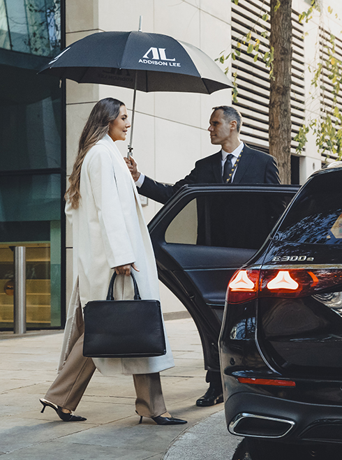 Chauffeur holding an umbrella for a woman getting into an Addison Lee taxi in London