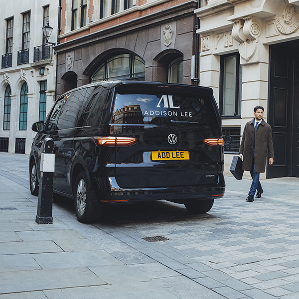 Man going into an Addison Lee multivan in the city of London wearing a coat and briefcase