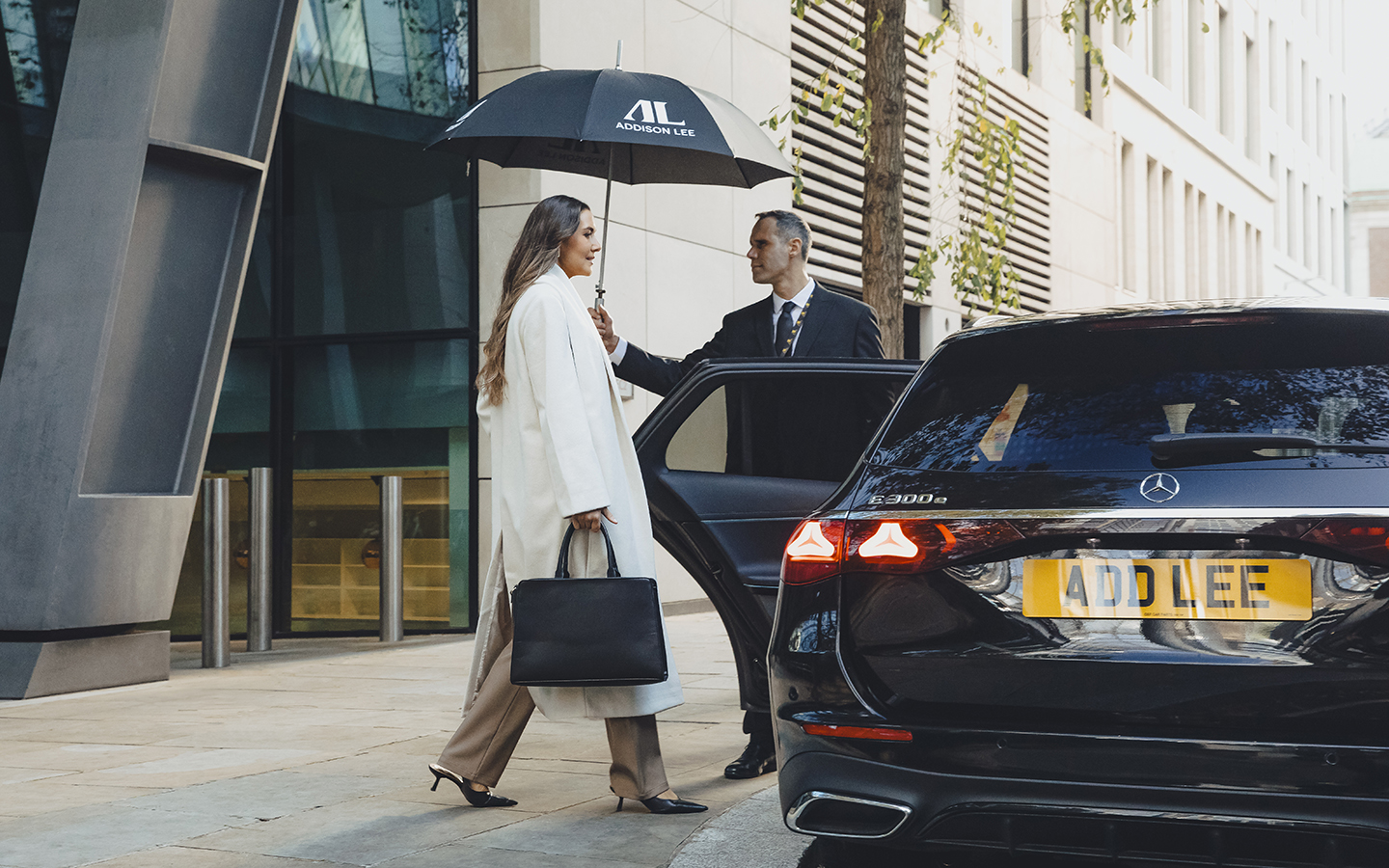 Chauffeur holding umbrella for a woman getting into an Addison Lee executive vehicle
