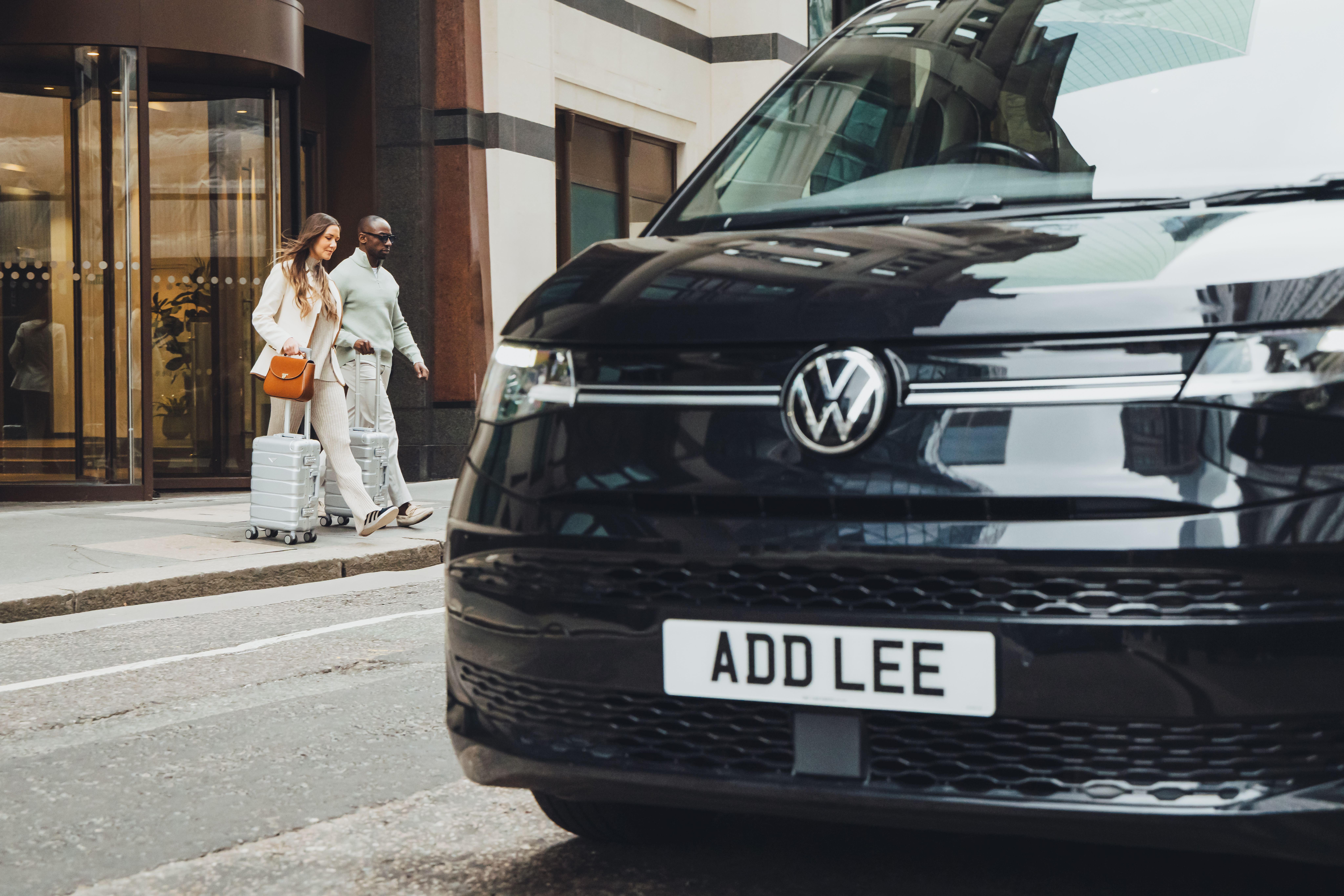 A couple with a suitcase walking into an Addison Lee taxi to go to the airport