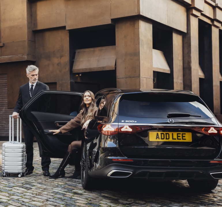Woman getting out of an executive car with an Addison Lee driver holding the door open for her and helping with her luggage