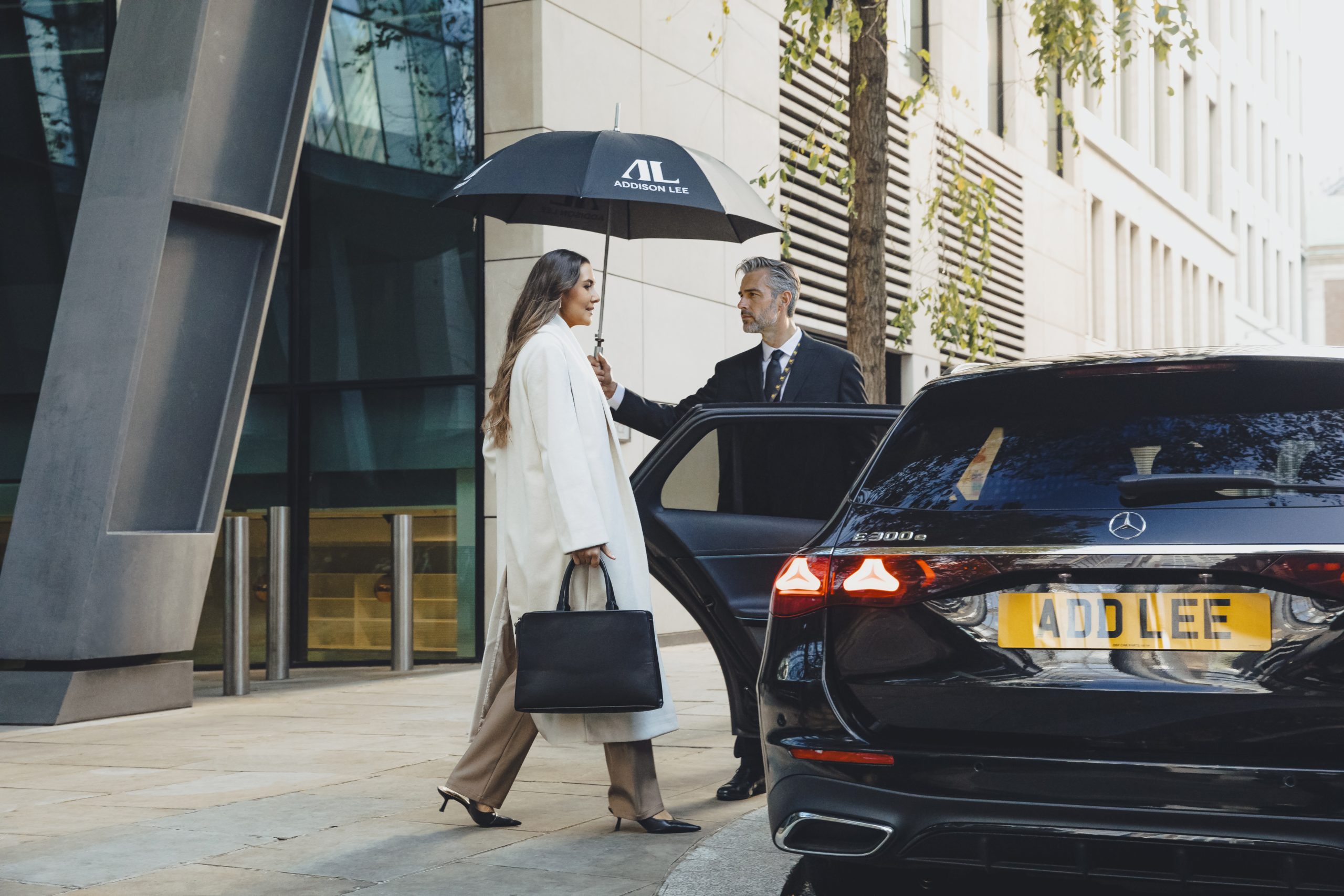 Woman getting into an Executive Addison Lee taxi while a chauffeur holds an umbrella for her and opens the car door