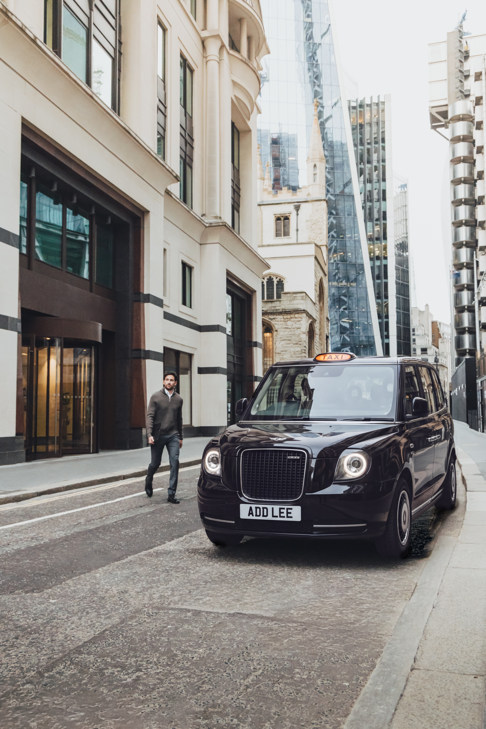 Man walking into an Addison Lee black taxi in the city of London